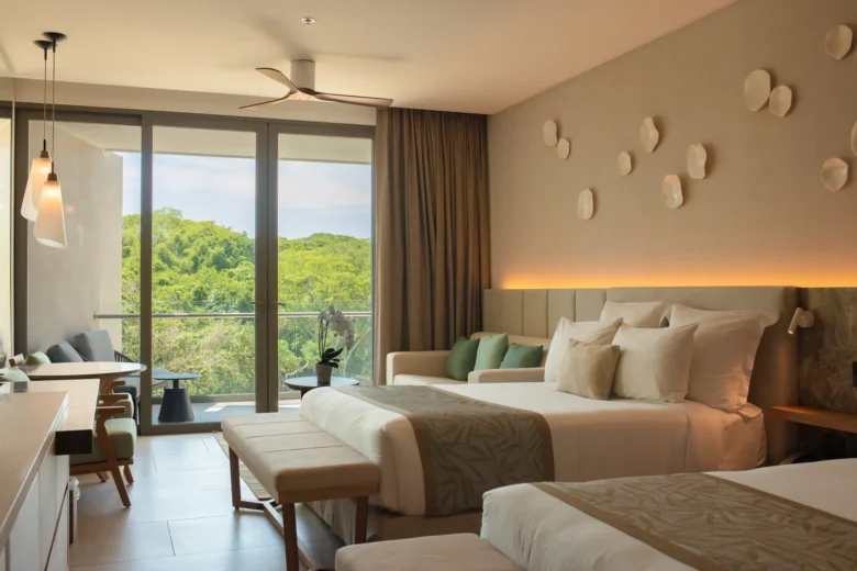 Family Suite Tropical View bedroom with two queen beds and balcony overlooking lush greenery at Dreams Bahia Mita Resort.
